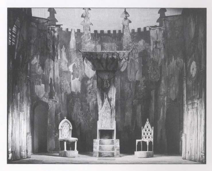 Black and white photograph of a set model showing three thrones of different designs.